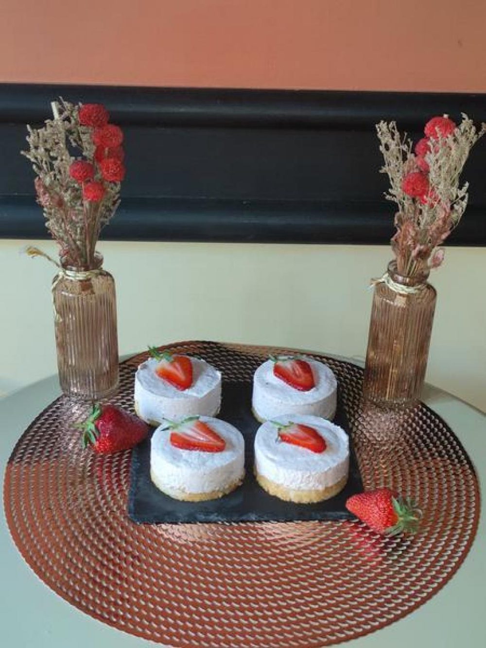 Quatre petits gâteaux aux fraises sur un plateau cuivré, entre deux vases de fleurs séchées